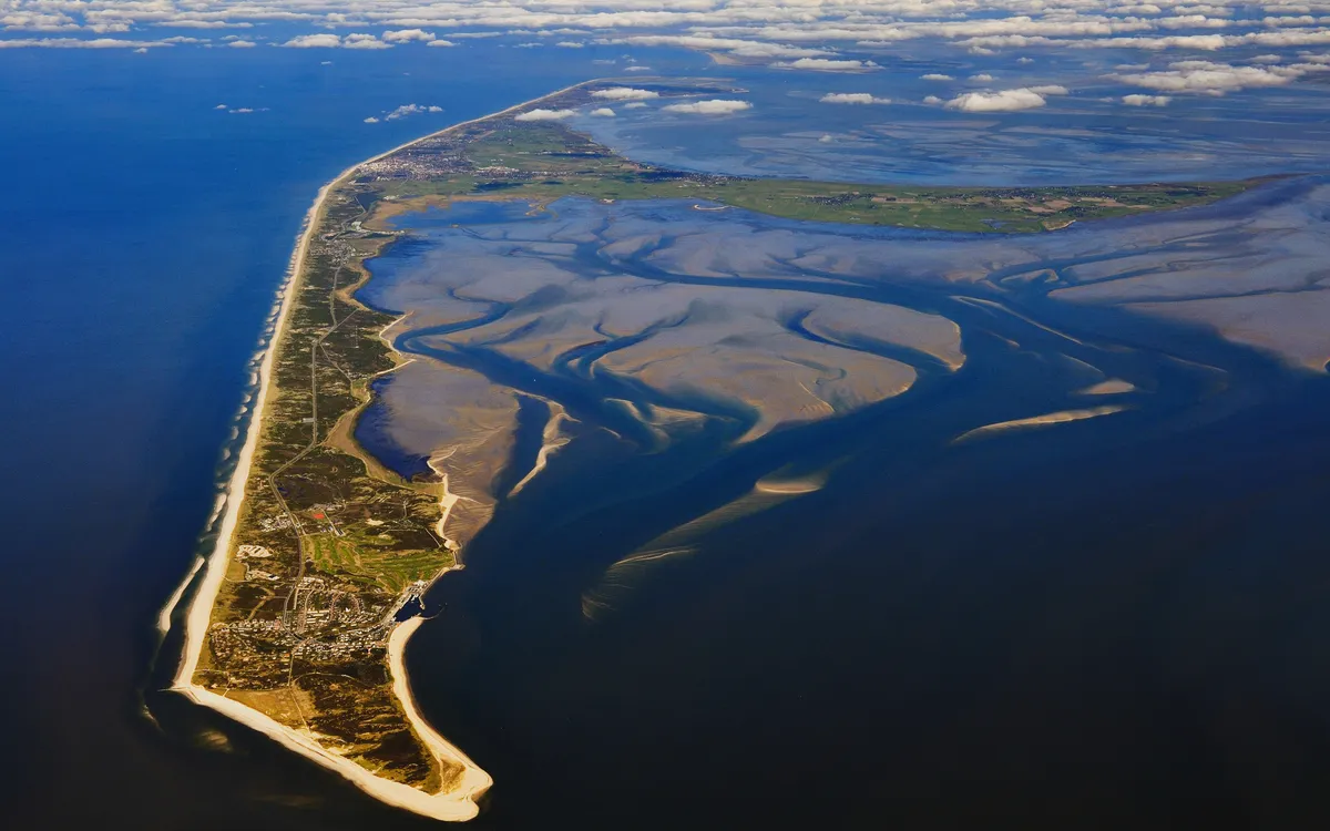 Luftaufnahme einer Küstenlandschaft mit Sandbänken und Feldern.