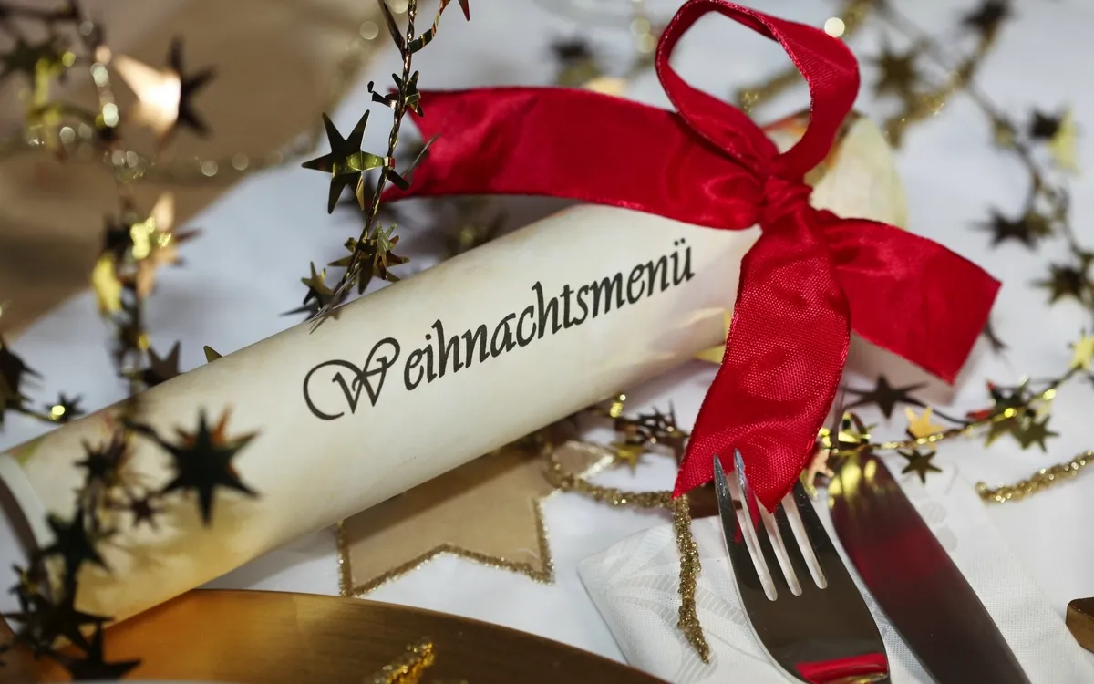 Weihnachtsmenürolle mit roter Schleife und Besteck auf dekoriertem Tisch.