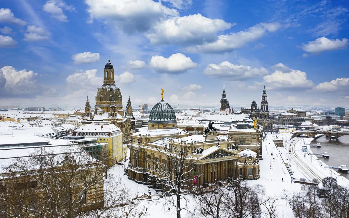 Winterliches Dresden mit der verschneiten Frauenkirche und der Elbe im Hintergrund.
