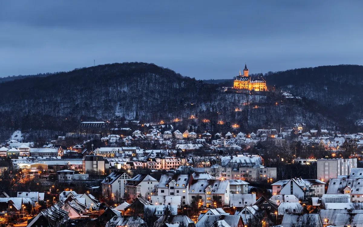 Winterliche Stadtansicht mit beleuchtetem Schloss auf einem Hügel.