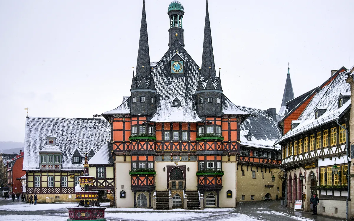 Verschneites Fachwerk-Rathaus mit Türmen und Marktbrunnen in einer Altstadt.