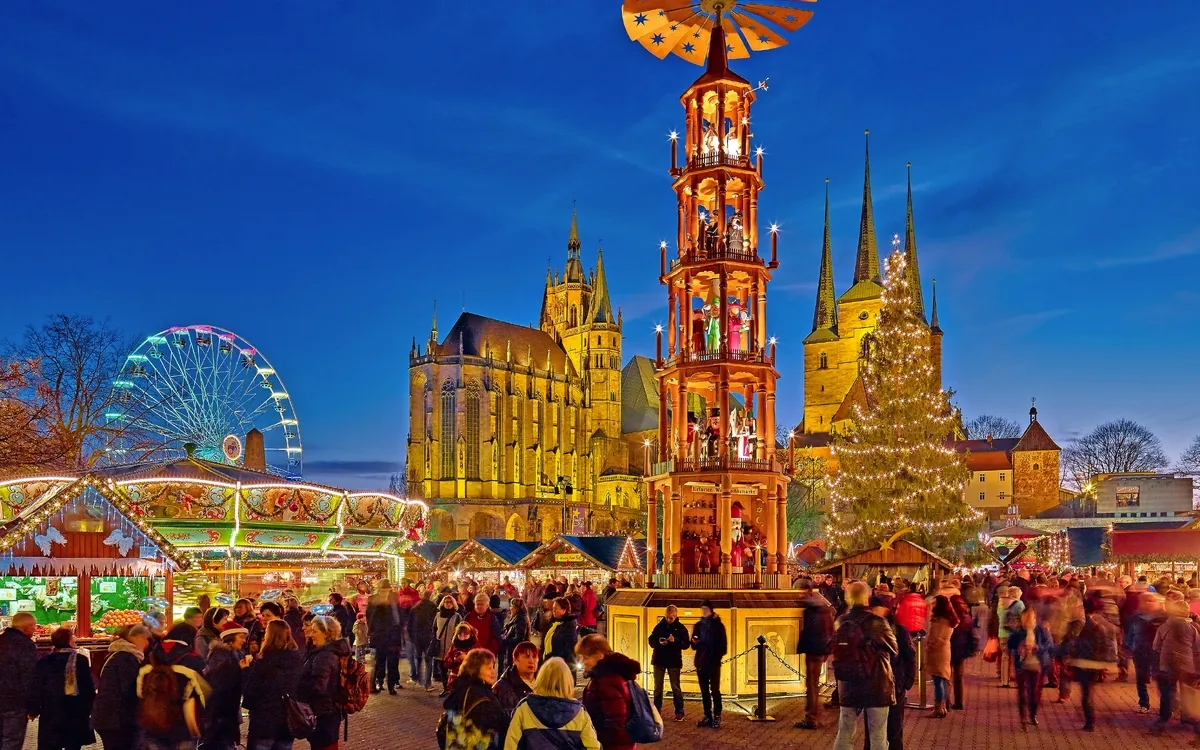 Menschen auf einem festlichen Weihnachtsmarkt bei Nacht mit Lichtern und Attraktionen.
