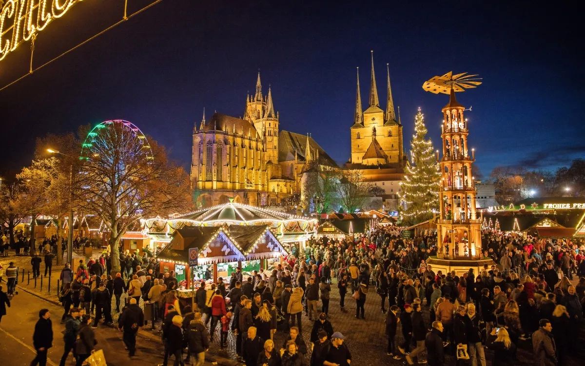 Menschen auf einem beleuchteten Weihnachtsmarkt in Erfurt bei Nacht.