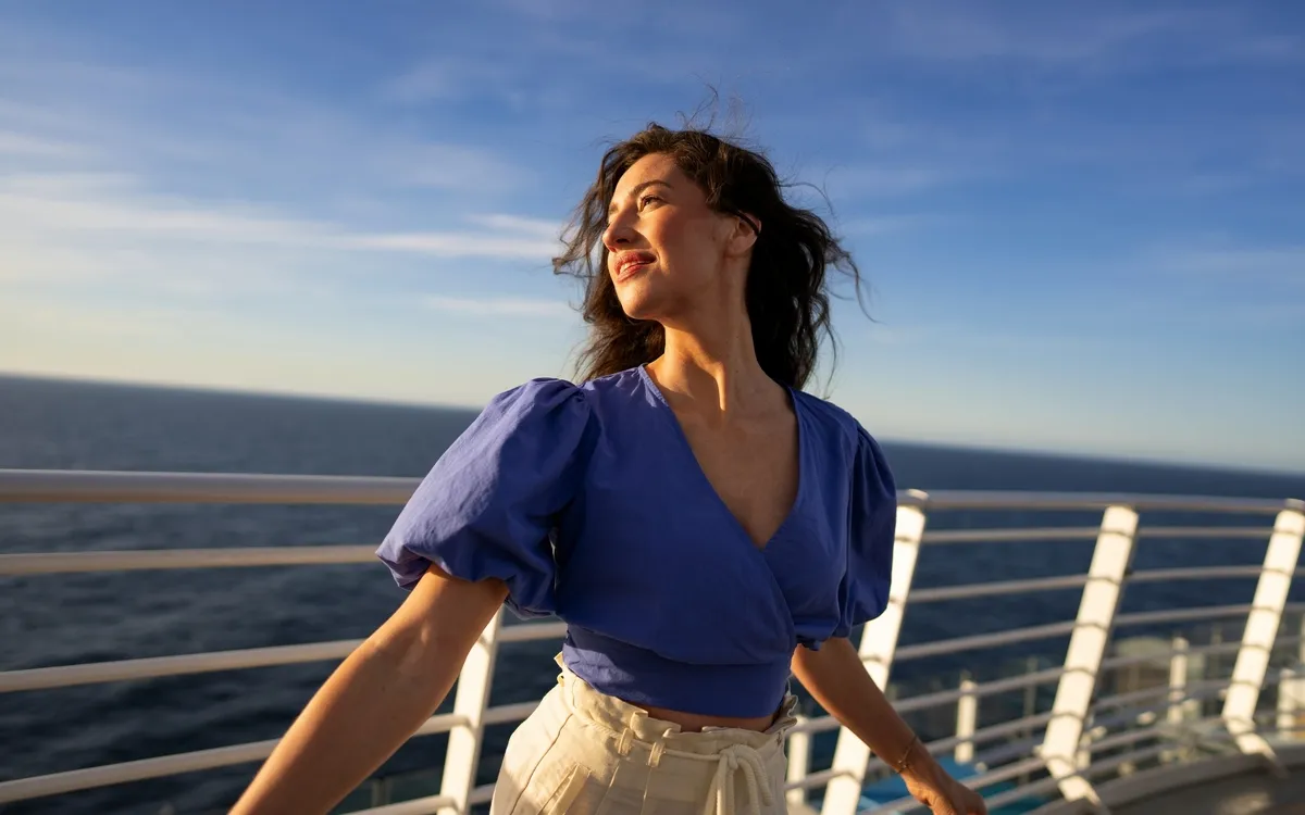 Frau auf einem Kreuzfahrtschiff, lächelnd im Sonnenschein auf dem Deck.