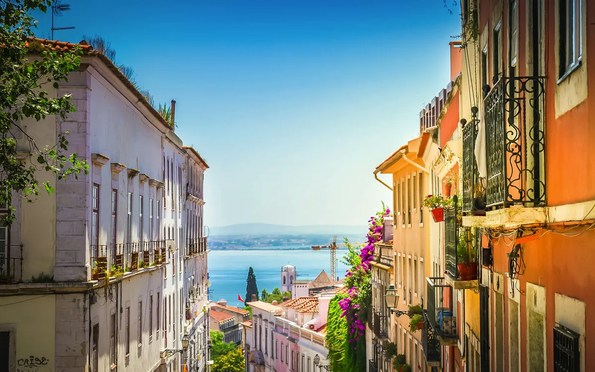 Blick auf eine enge, farbenfrohe Gasse mit Meer im Hintergrund.