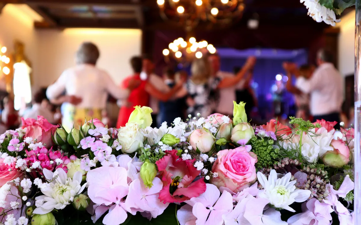 Blumenarrangement im Vordergrund, unscharfe tanzende Menschen im Hintergrund.