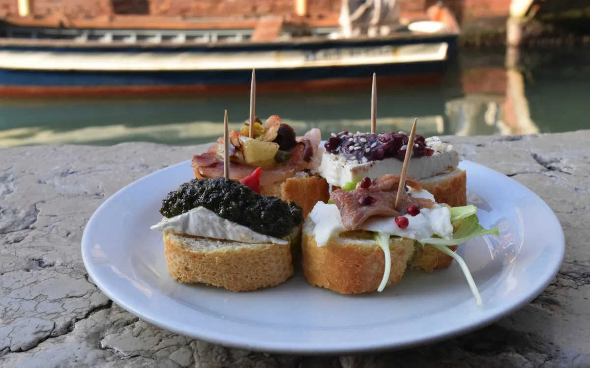 Teller mit belegten Baguettescheiben vor einem Boot auf dem Wasser.