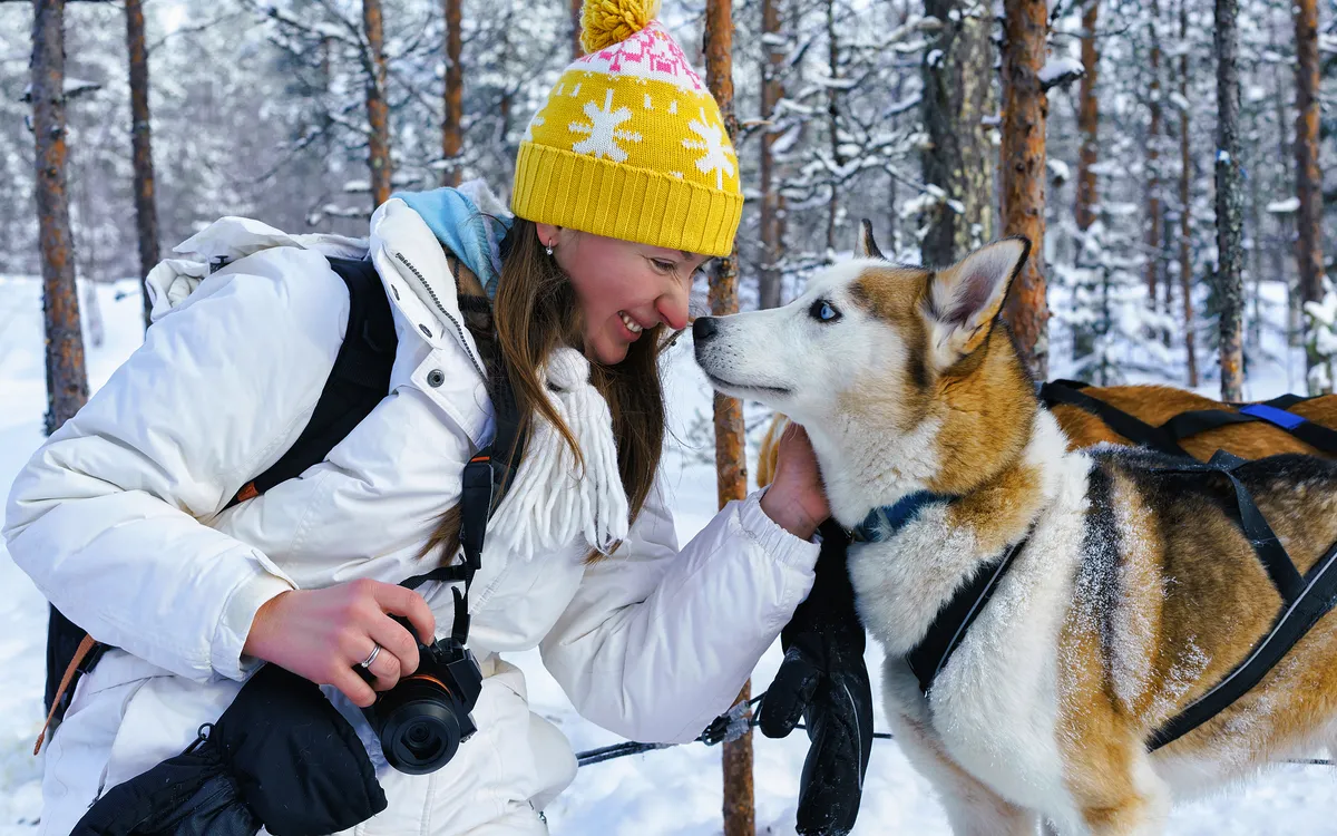 Frau im Schnee mit Hund in winterlichem Wald.