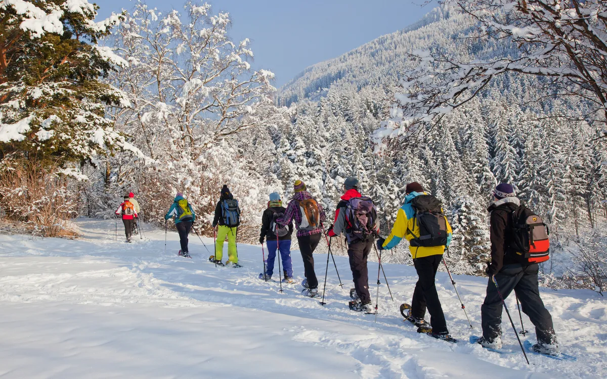Gruppe von Menschen beim Schneeschuhwandern durch eine verschneite Winterlandschaft in den Bergen.