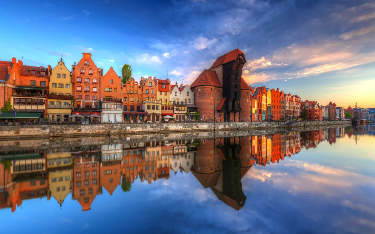 Bunte Gebäude spiegeln sich im Wasser eines Flusses bei Sonnenuntergang.