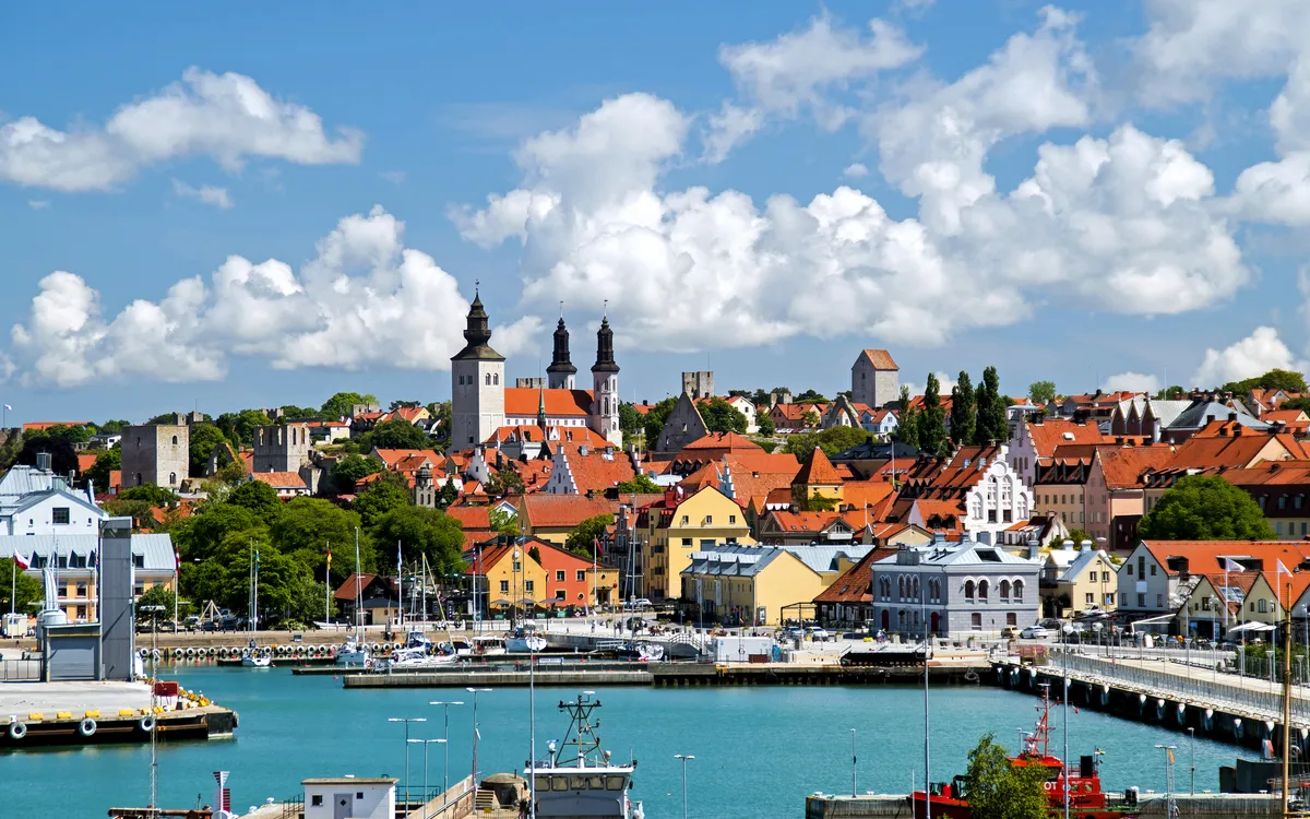 Hafenstadt mit farbenfrohen Gebäuden und Kirchtürmen im Hintergrund, unter blauem Himmel.