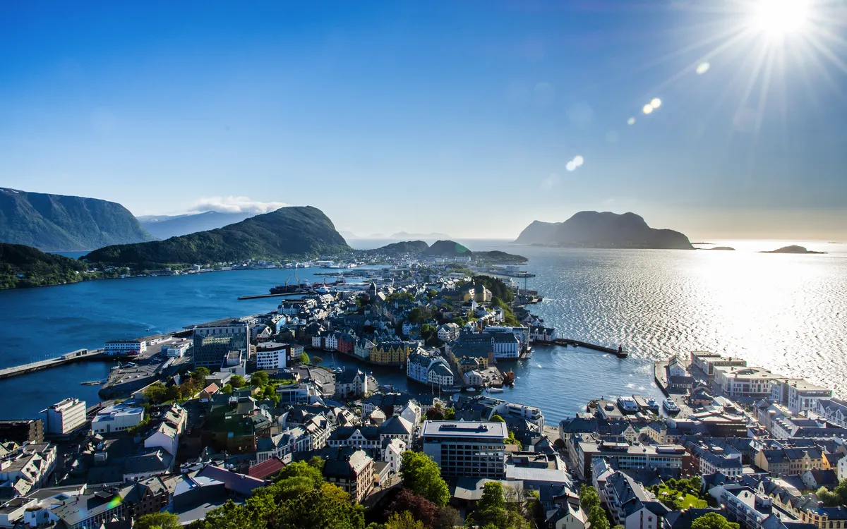 Küstenstadt mit Bergen und Sonne im Hintergrund.