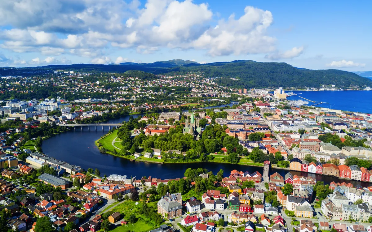 Luftaufnahme einer Stadt mit Fluss und Brücke, umgeben von grüner Landschaft.