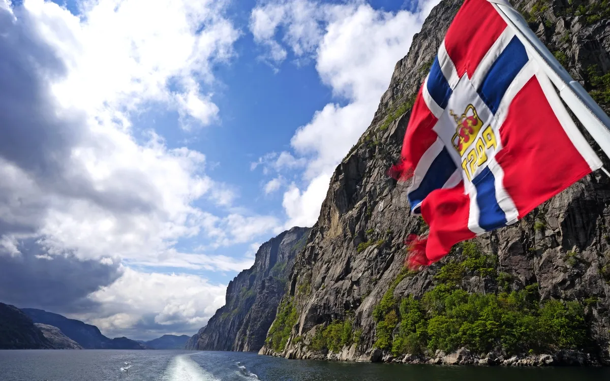 Norwegische Flagge im Lysefjord mit steilen Felswänden und Himmel.