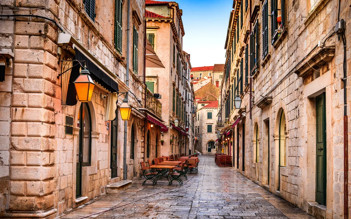 Gepflasterte Altstadtgasse mit Terrassencafé und historischen Gebäuden.