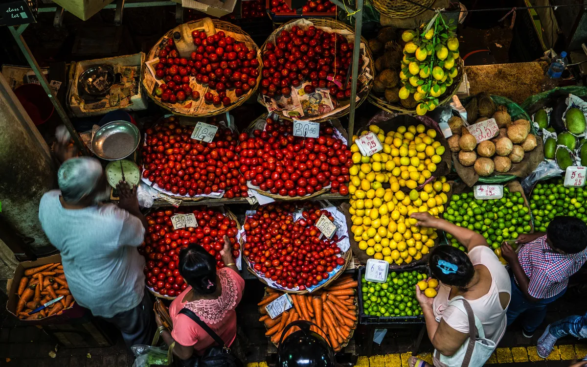 Menschen kaufen buntes Obst und Gemüse auf einem belebten Markt.