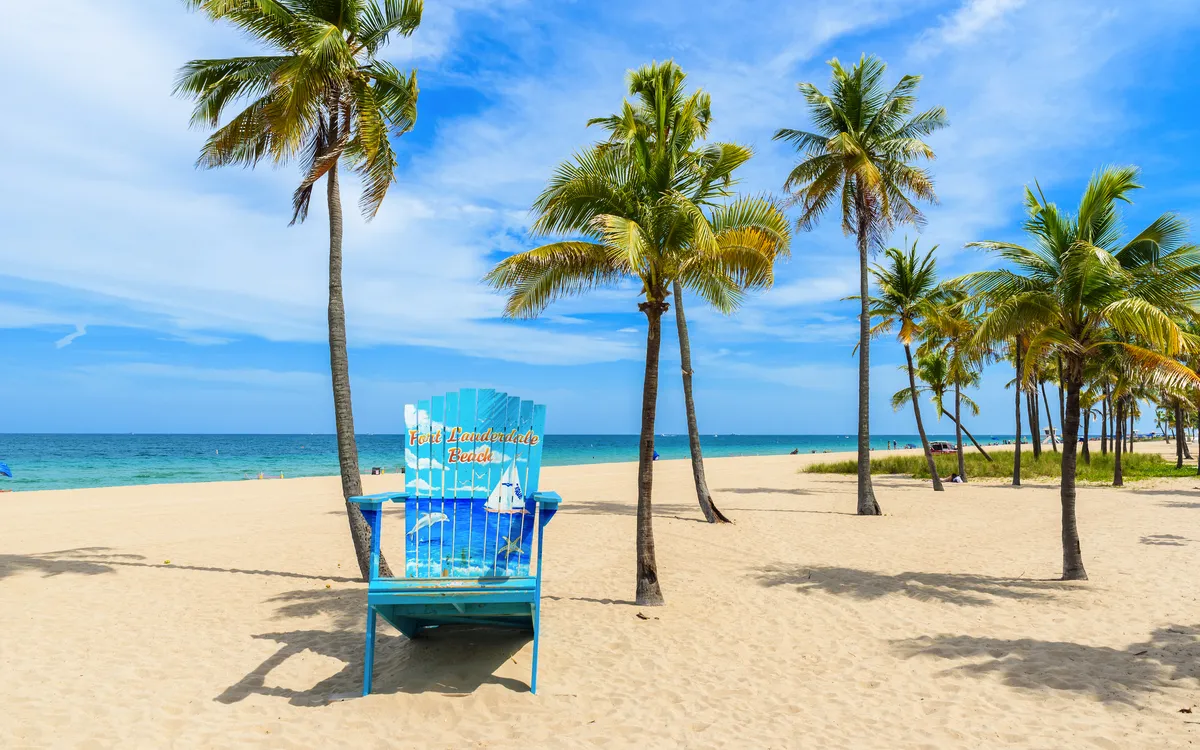 Blauer großer Strandstuhl und Palmen auf einem sonnigen Sandstrand.