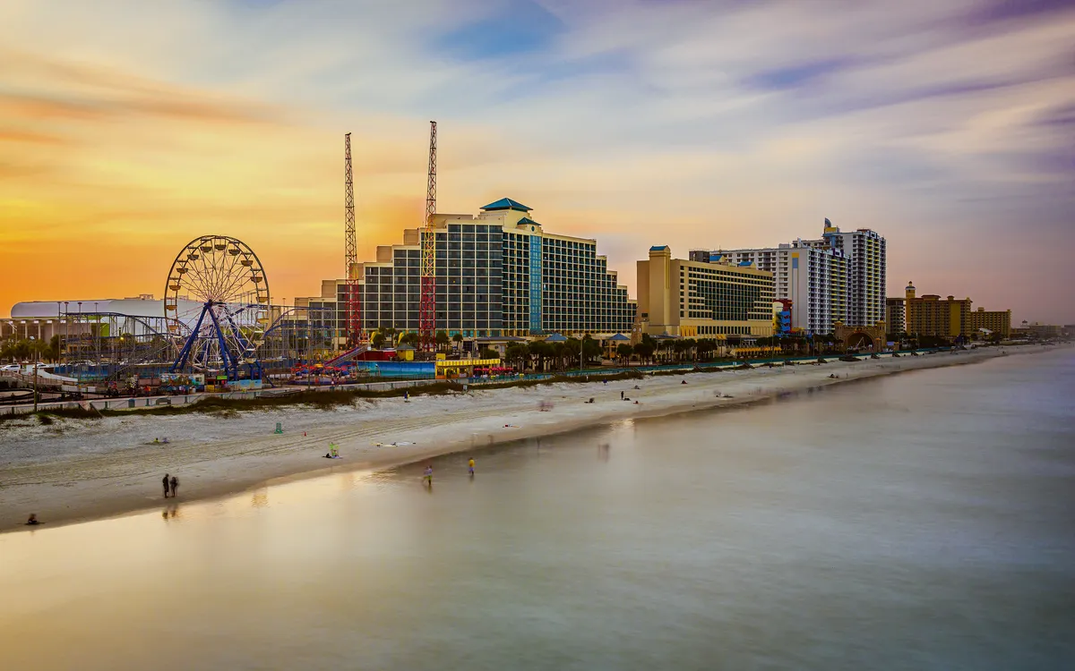 Strandpromenade mit Hochhäusern bei Sonnenuntergang, Riesenrad im Hintergrund.