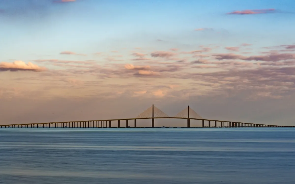Eine lange Brücke über das ruhige Meer bei Sonnenuntergang.