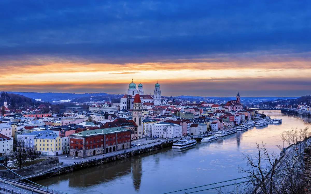 Stadtansicht mit Fluss und Sonnenuntergang im Hintergrund.