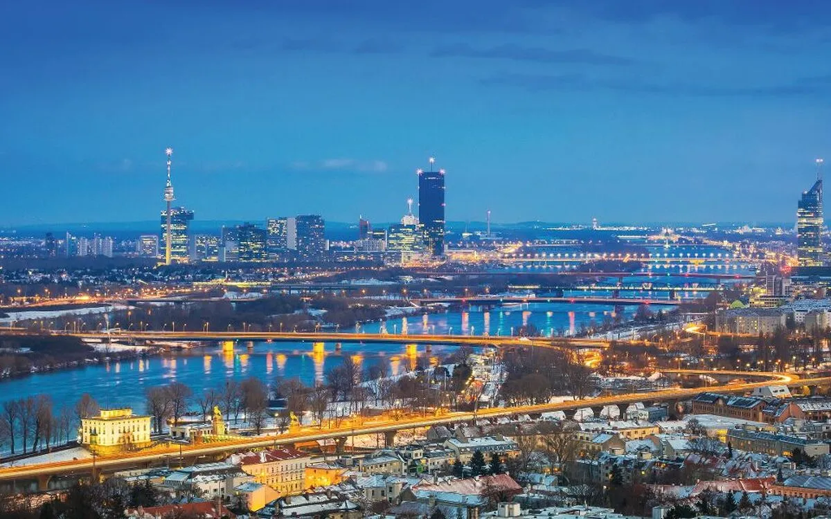 Stadtpanorama von Wien bei Dämmerung mit beleuchteten Brücken und Donau.