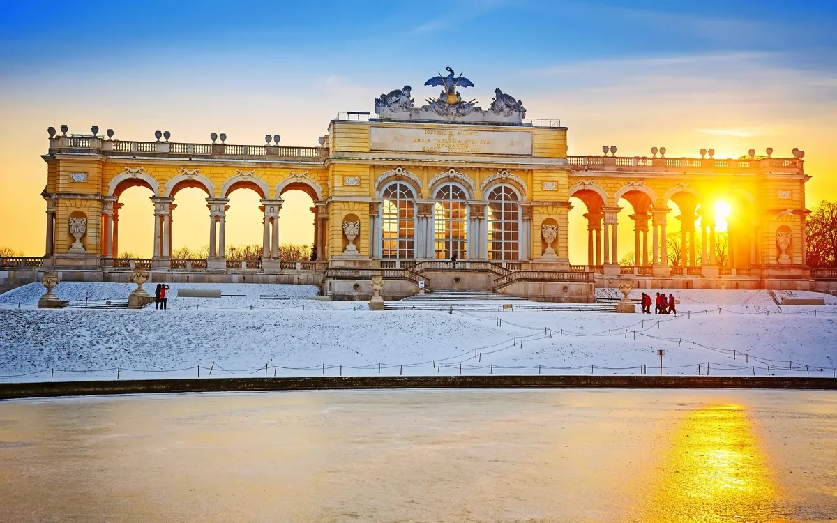 Gloriette im Schlossgarten Schönbrunn im Winter mit Schnee und Sonnenuntergang.