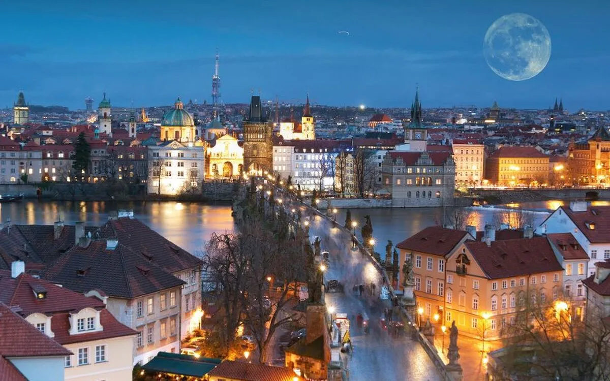 Prag bei Nacht mit beleuchteter Karlsbrücke und Vollmond im Hintergrund
