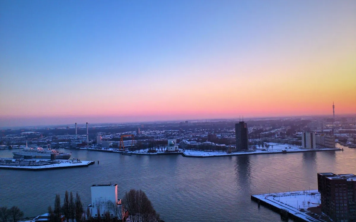 Stadtpanorama mit Fluss im Sonnenuntergang, schneebedeckte Gebäude und bunte Himmel.