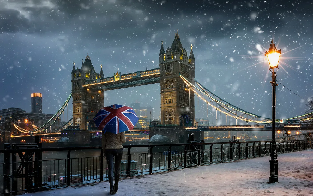 Tourist mit Schirm vor der Tower Bridge im Schnee in London.