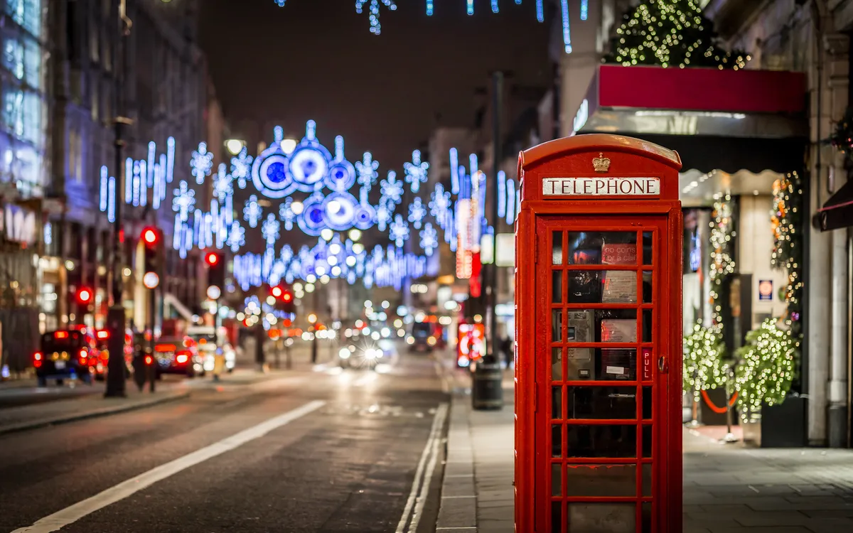 Rote Telefonzelle bei Nacht, umgeben von festlicher Straßenbeleuchtung.