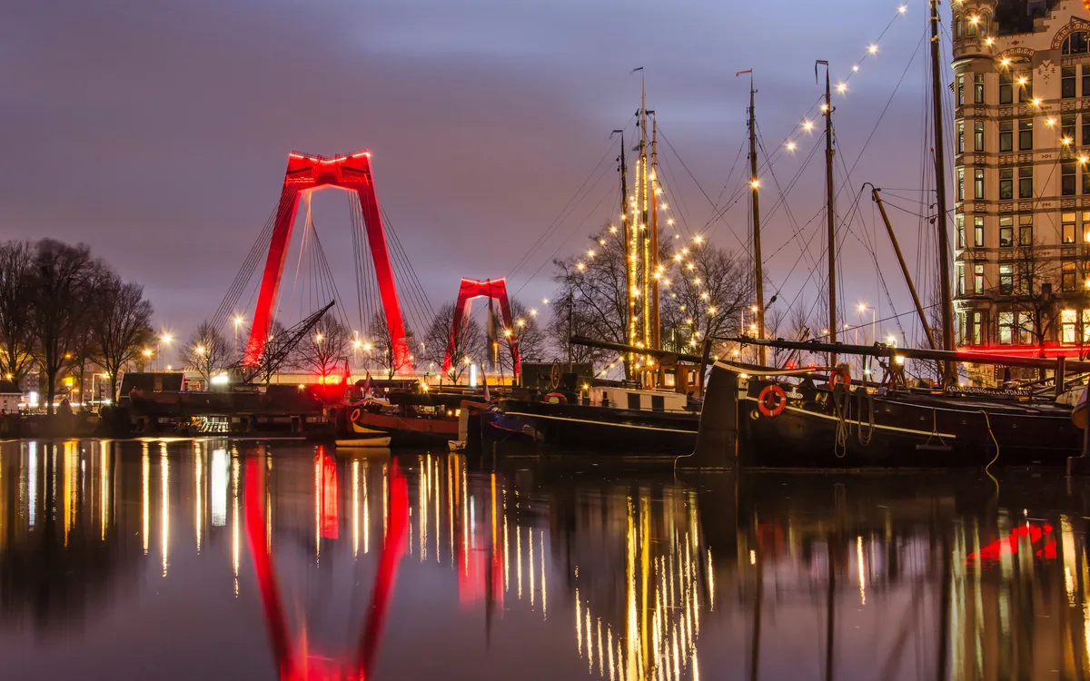 Alter Hafen in Rotterdam am Morgen mit Lastkähnen und Willemsbrücke im Hintergrund.