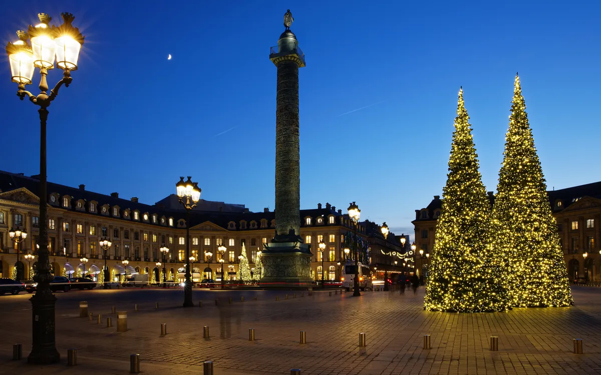 Beleuchtete Weihnachtsbäume und Säule auf einem städtischen Platz bei Dämmerung.
