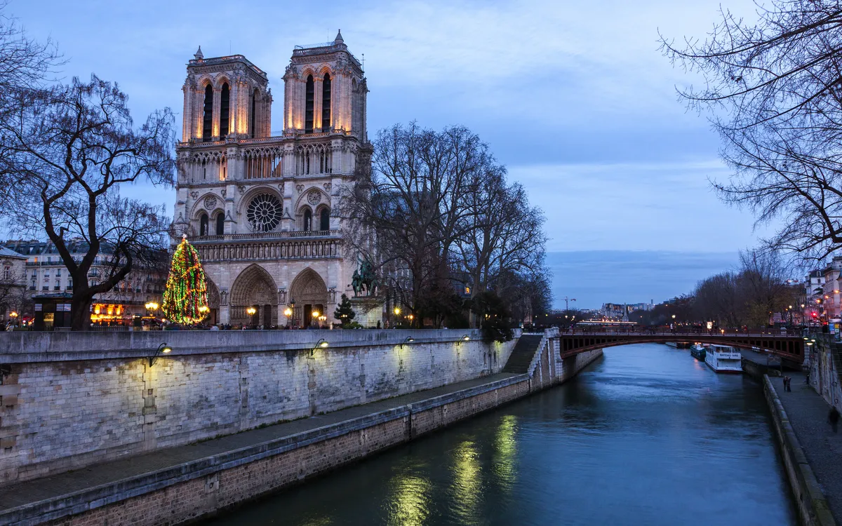 Notre-Dame de Paris bei Dämmerung, Lichter erleuchten die Fassade, Fluss im Vordergrund.