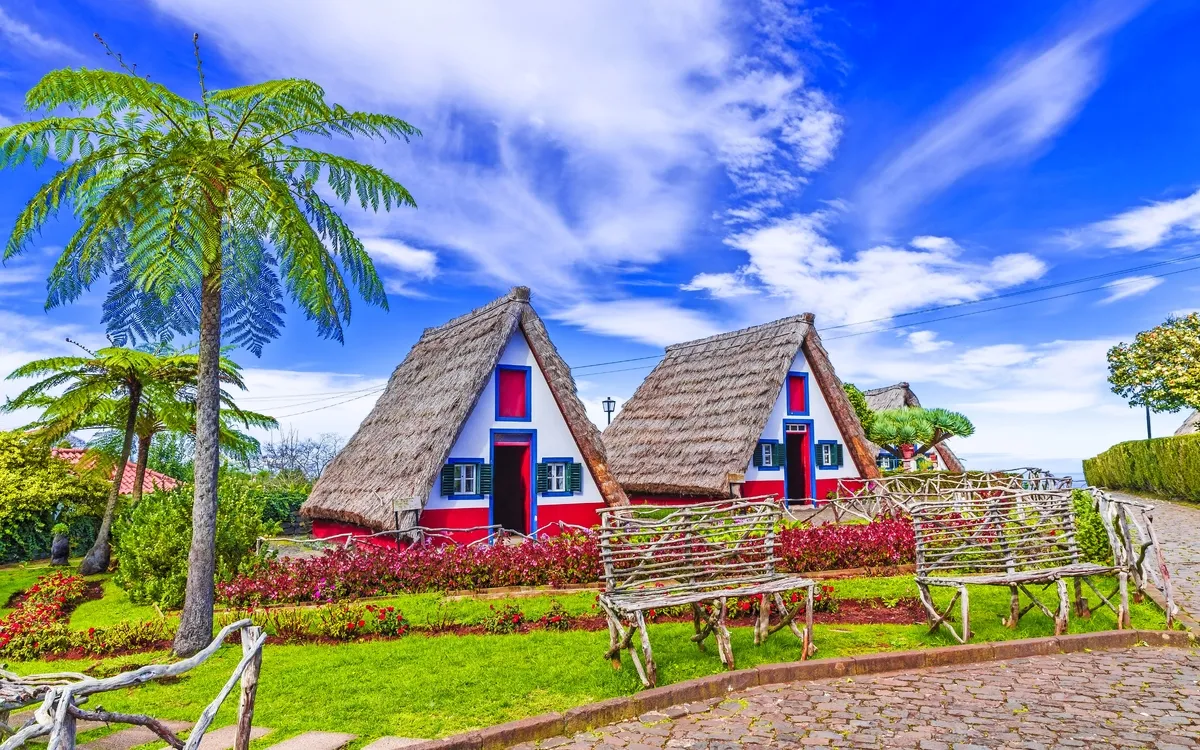 Traditionelle Reetdachhäuser in Santana, Madeira, umgeben von üppigem Garten.
