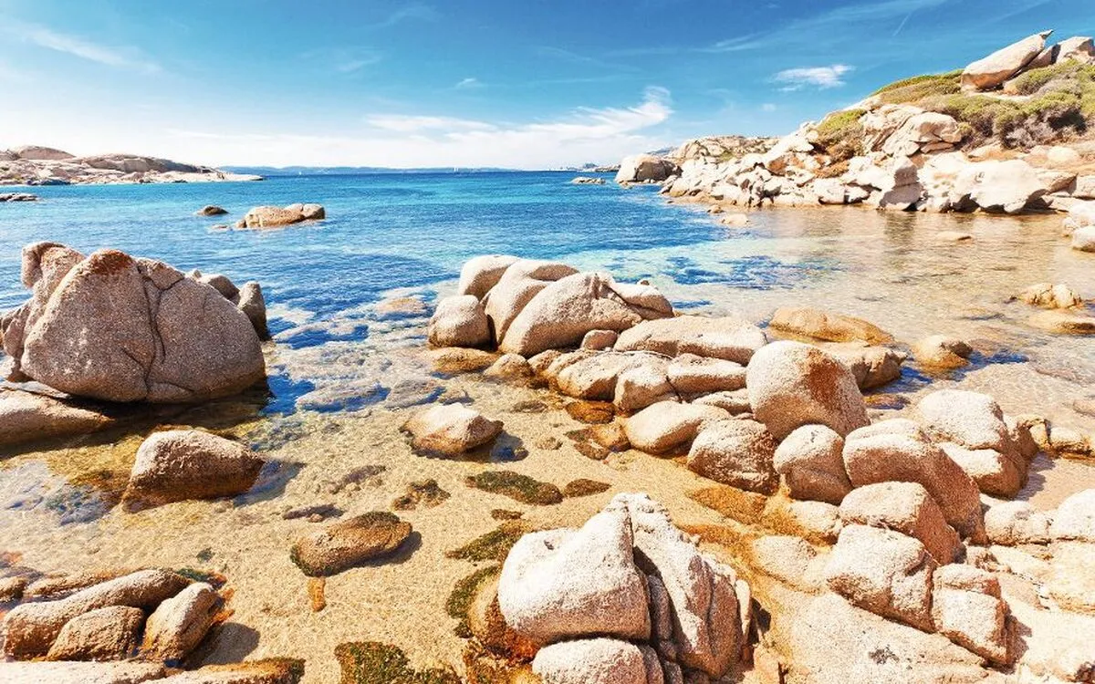 Felsige Küstenlandschaft mit klarem blauem Wasser und hellem Himmel im Hintergrund.