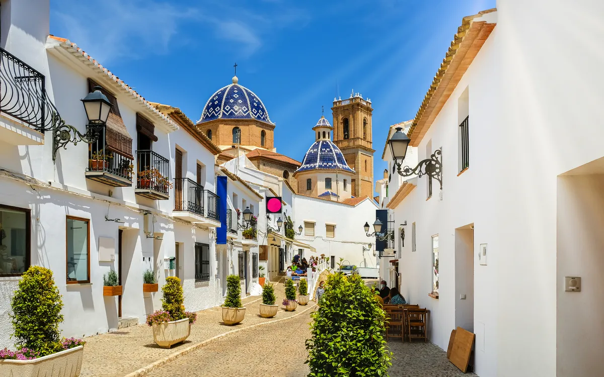 Straße in Altea mit weiß getünchten Häusern und blauen Kirchenkuppeln.