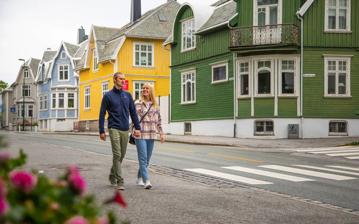 Ein Mann und eine Frau spazieren in Kristiansund entlang bunter Häuser.