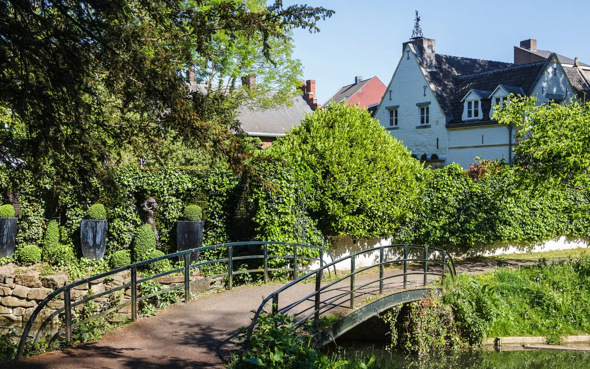 Kleine Brücke in einem grünen Garten vor alten Häusern.