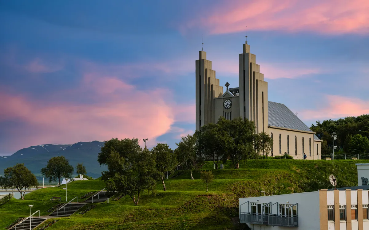 Kirche auf Hügel mit Bäumen und rosa Himmel im Hintergrund.