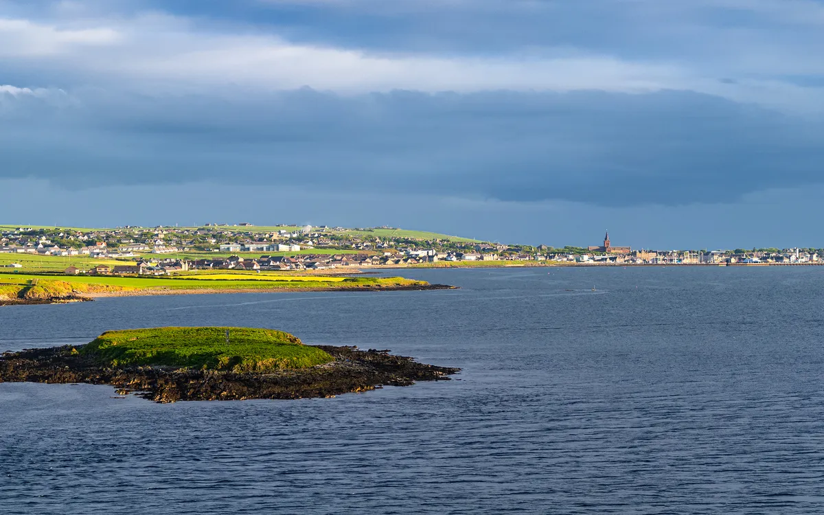 Insel im Meer mit Stadt im Hintergrund bei bewölktem Himmel