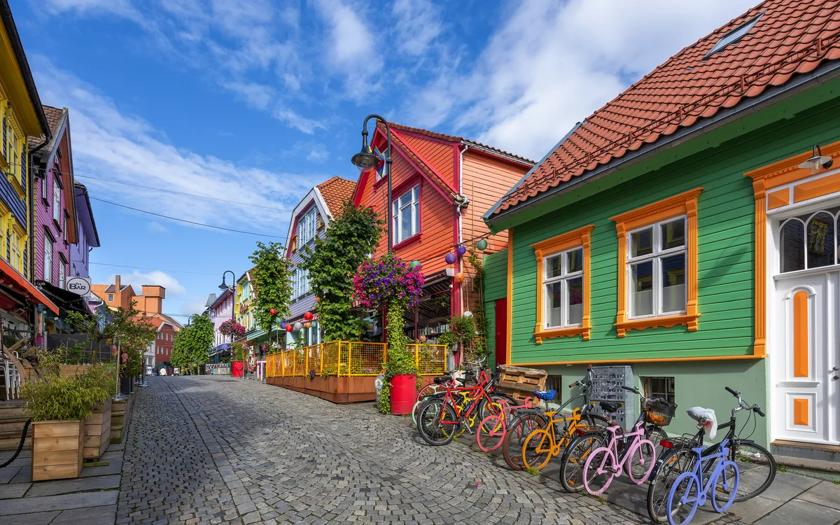 Bunte Häuserzeile mit Fahrrädern in kopfsteingepflasterter Straße bei blauem Himmel.