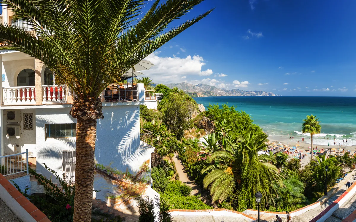 Ausblick auf Strand und Meer mit Palmen und mediterraner Architektur.