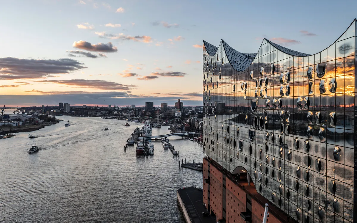 Blick auf die Elbphilharmonie in Hamburg bei Sonnenuntergang, Hafen und Elbe im Hintergrund.