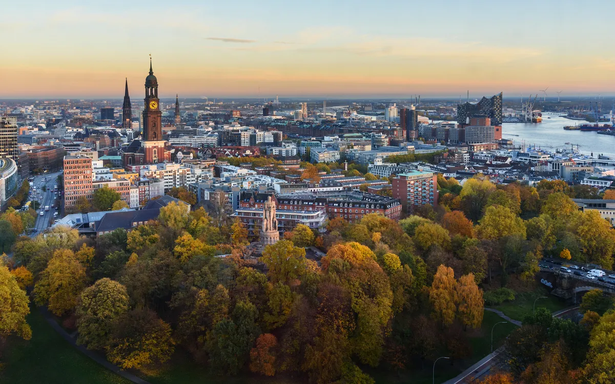 Stadtansicht von Hamburg mit Herbstbäumen und Elbphilharmonie im Hintergrund.