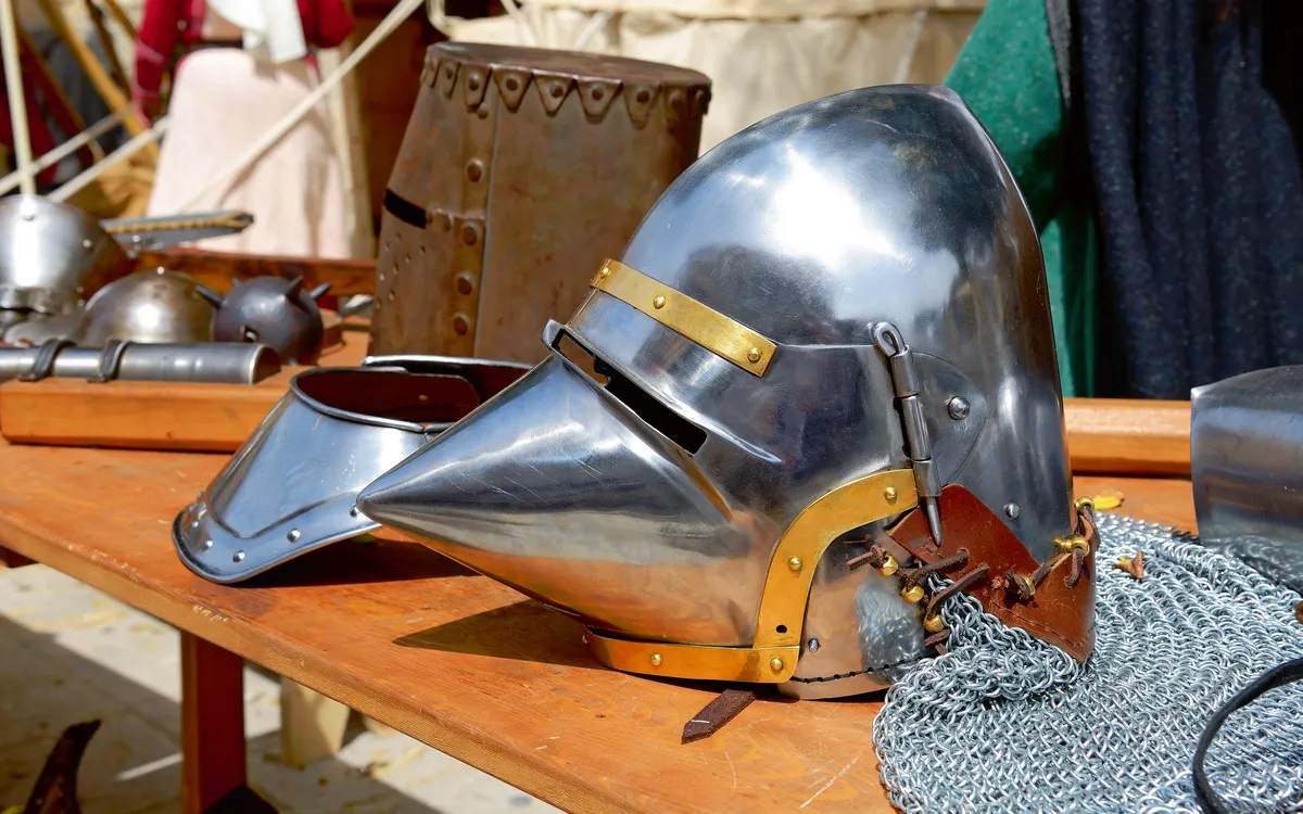 Ritterhelm aus Metall mit Kettenhemd auf Holztisch.