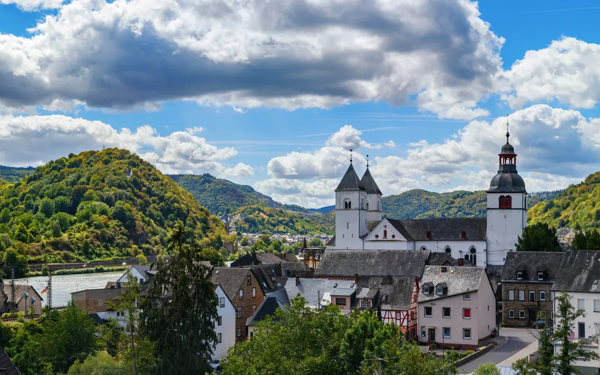 Panorama einer malerischen Kleinstadt am Fluss mit Hügeln im Hintergrund.