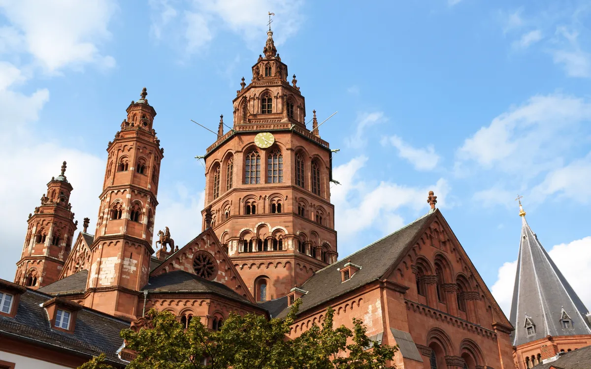Backstein-Kathedrale mit markanten Türmen und einer Uhr an der Fassade unter blauem Himmel.