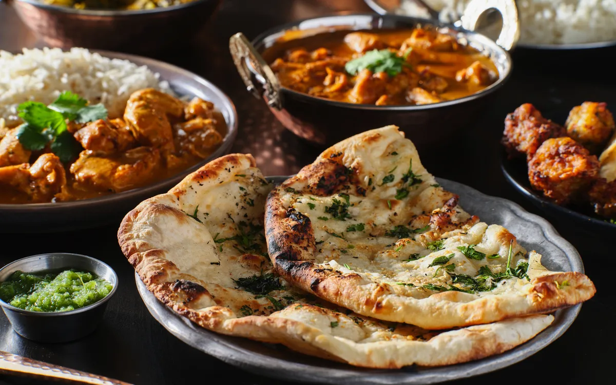 Indisches Essen mit Curry, Reis und Naanbrot auf einem Tisch serviert.